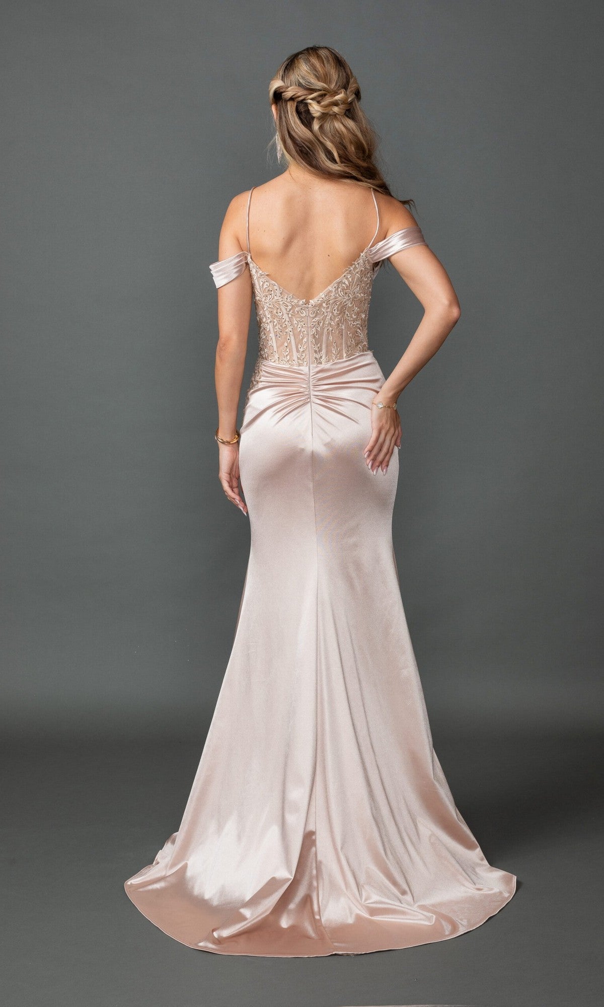 A woman with long wavy hair models the Dancing Queen 4537, a floor-length, off-the-shoulder light pink satin prom dress with a fitted bodice and lace embroidery, posing with her back to the camera against a plain background.
